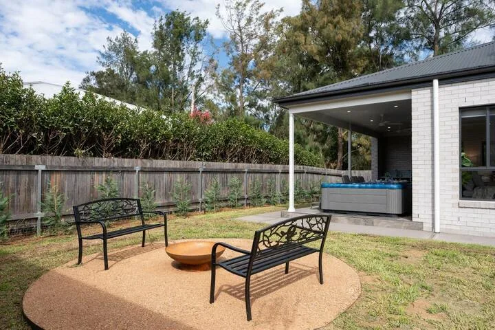 A backyard seating area with benches and an outdoor spa beside the house.