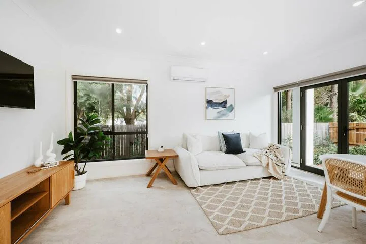 A bright living room with white seating, a patterned rug, and large windows.