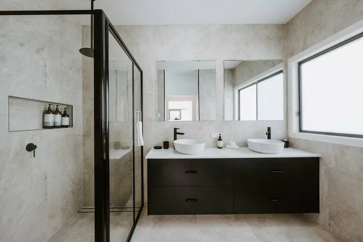 A bathroom with a glass shower and a dark double-sink vanity.