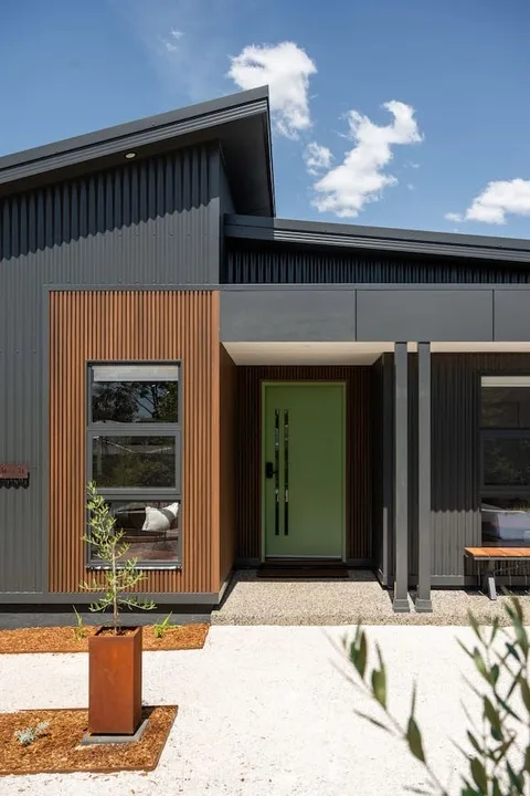 A modern house exterior with a green front door and a gravel walkway.