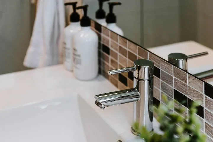 A bathroom sink with a chrome faucet and soap dispensers beside the mirror.