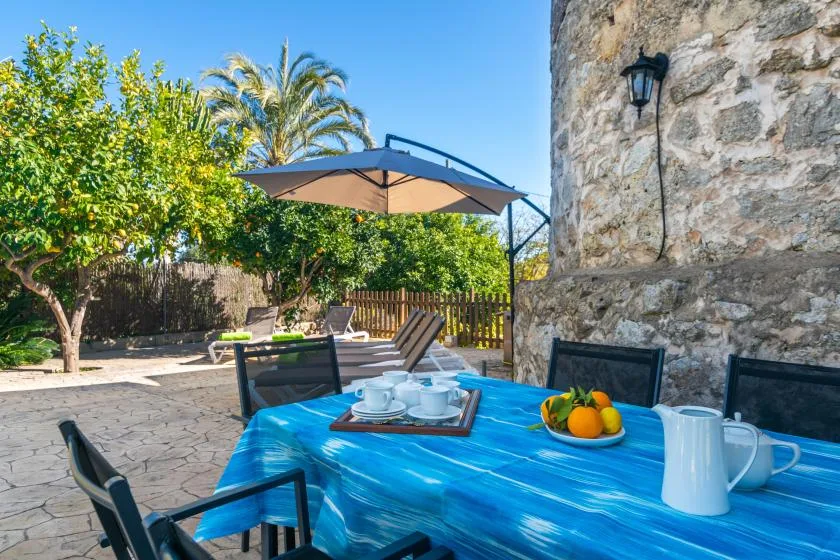 Una mesa azul al aire libre está junto a un muro de piedra en un jardín soleado.