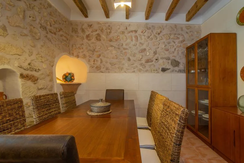 Un comedor con una mesa de madera, asientos tejidos y un armario con puertas de cristal.