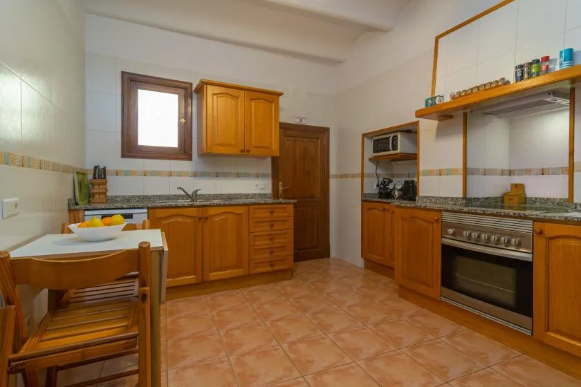 Una cocina con suelo de baldosas, armarios de madera, encimera y mesa de comedor.