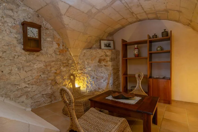 Una estancia de piedra rústica con una mesa de madera y asientos tejidos.