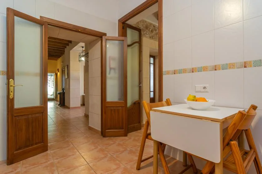 Comedor con una mesa blanca y asientos de madera junto a puertas interiores abiertas.