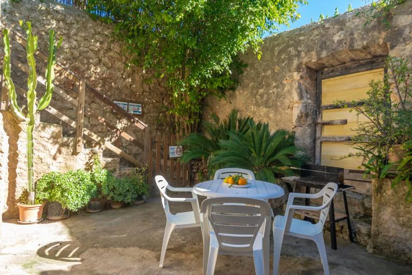 Un patio exterior con una mesa redonda y sillas blancas junto a muros de piedra.