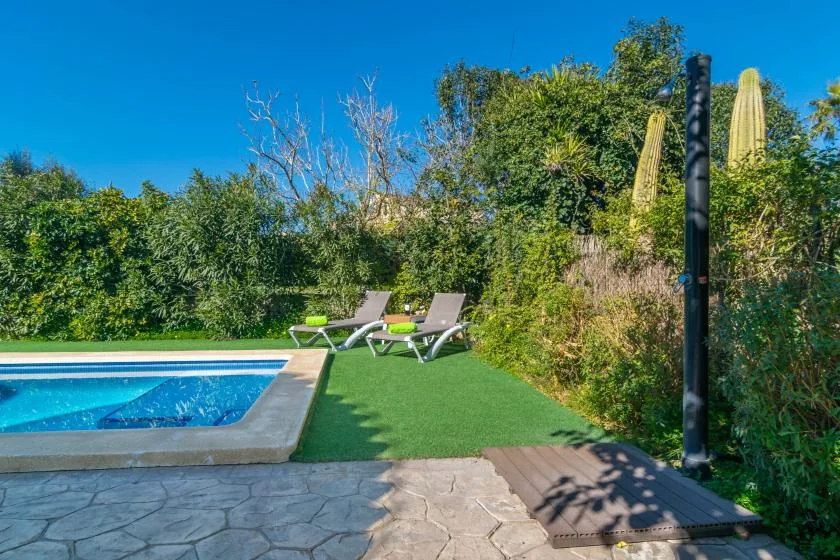 Una piscina al aire libre junto a asientos reclinables y césped verde.