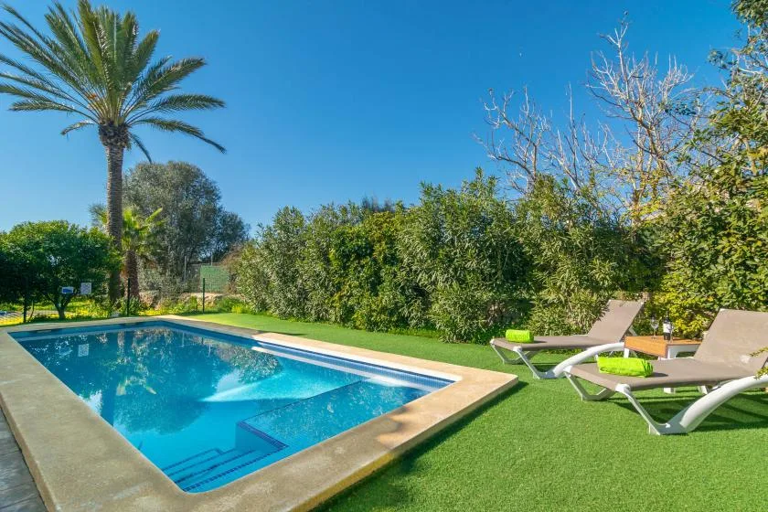 Una piscina al aire libre junto a un césped, setos y asientos de descanso.