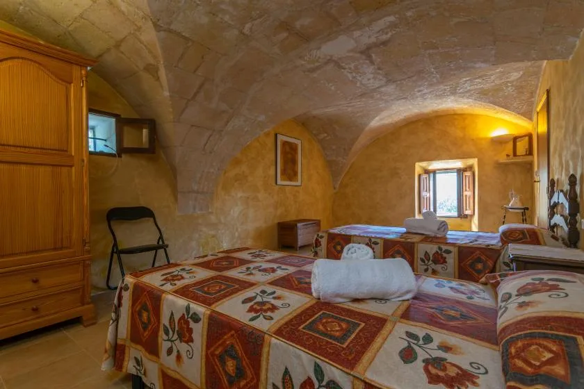 Dormitorio con techo abovedado de piedra, ropa de cama estampada y una ventana pequeña.