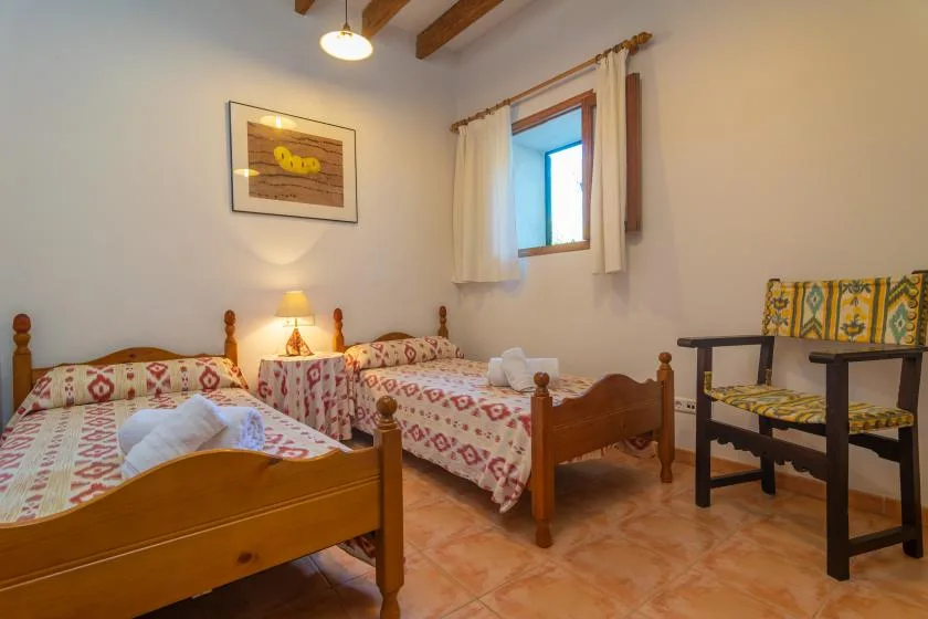 Un dormitorio con dos camas, una ventana pequeña y una silla de madera.
