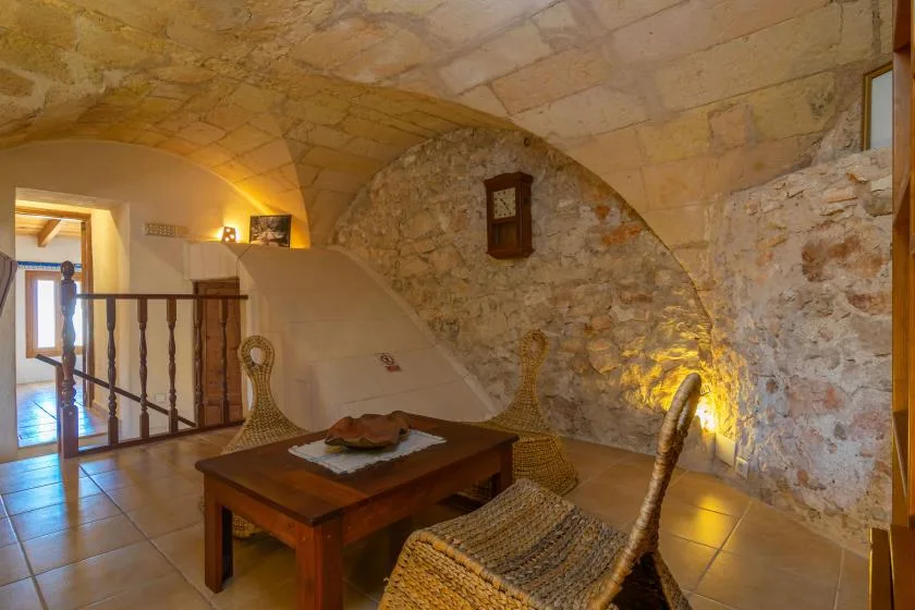 Una zona de estar con bóveda de piedra tiene asientos tejidos y una mesa de madera.