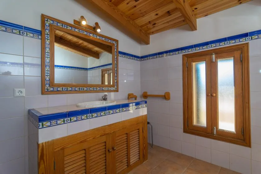 Un baño alicatado tiene un tocador de madera, un espejo y una ventana.