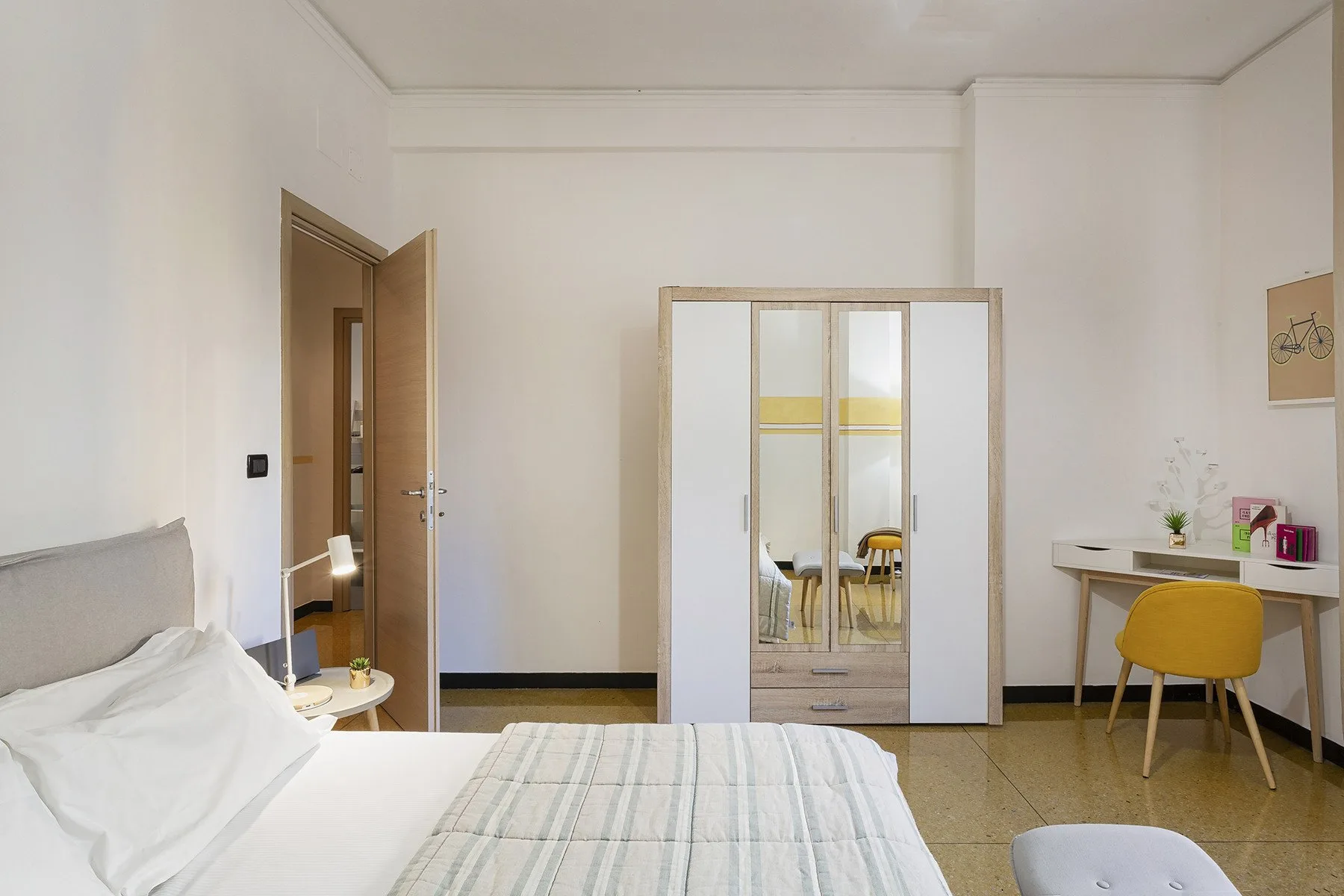 A bedroom with a bed, mirrored wardrobe, and small desk.