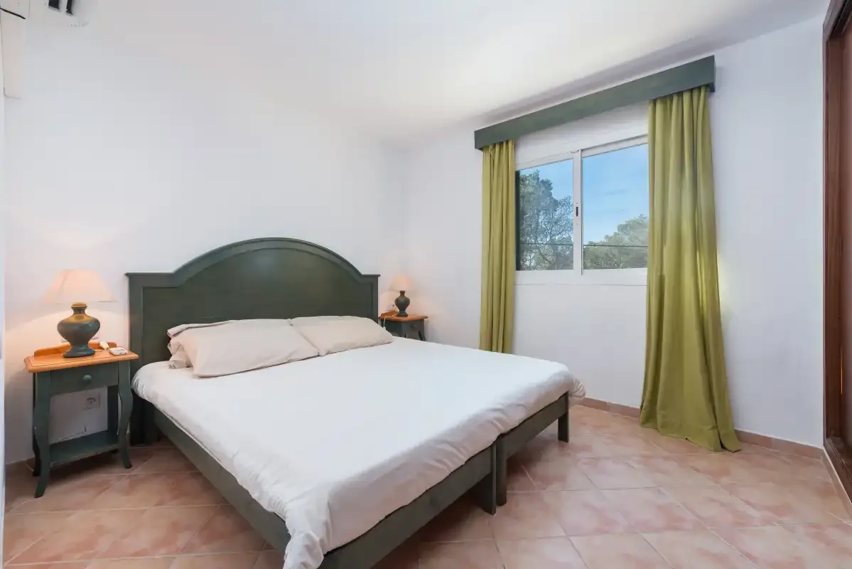 Un dormitorio con una cama doble y una ventana enmarcada por cortinas verdes.