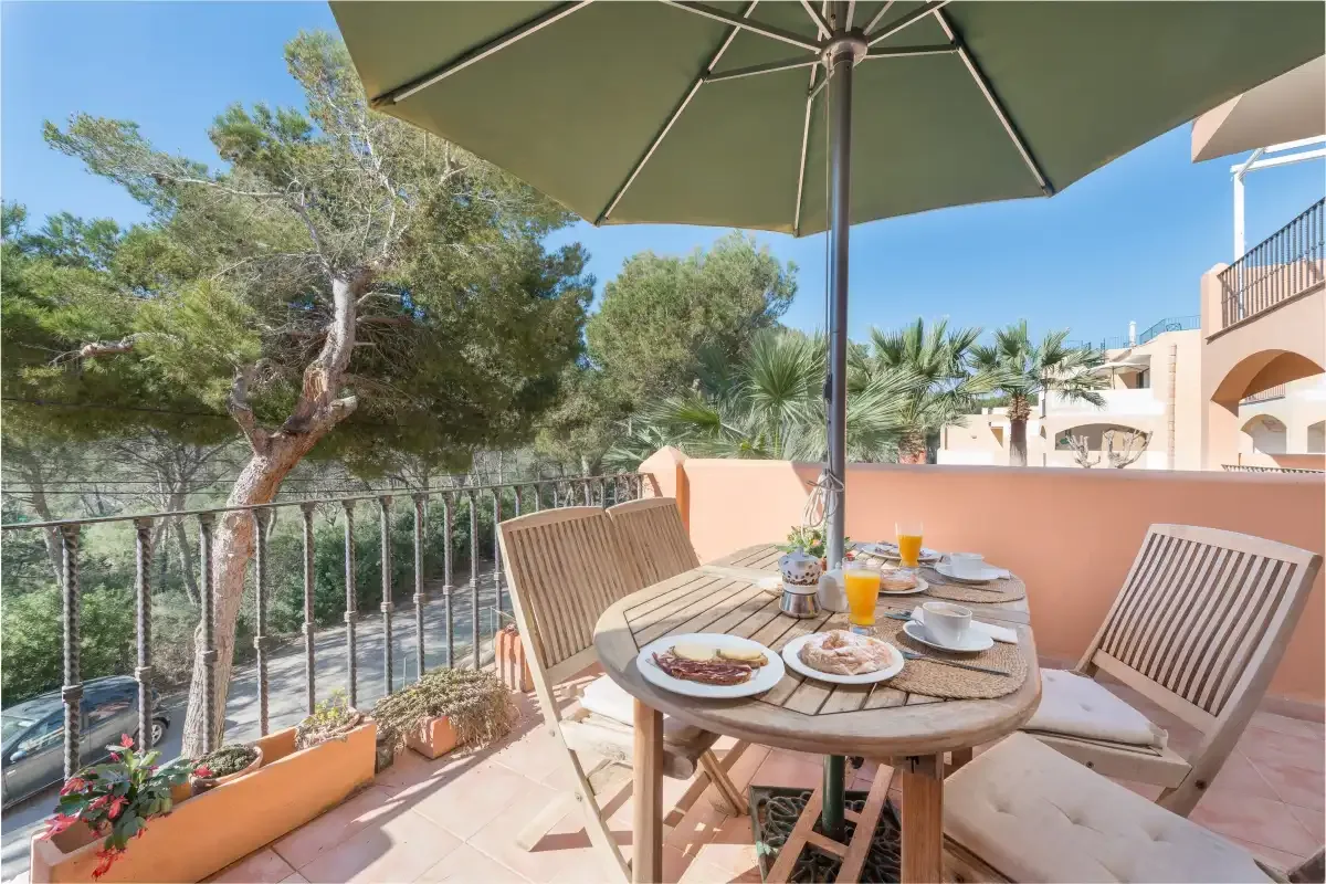 Una zona de comedor en la terraza con mesa, sillas y una sombrilla grande.