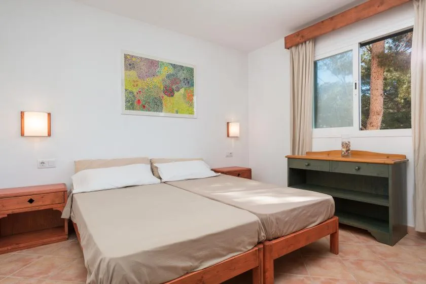 Un dormitorio con una cama doble, mesitas de noche y una ventana con vistas a los árboles.