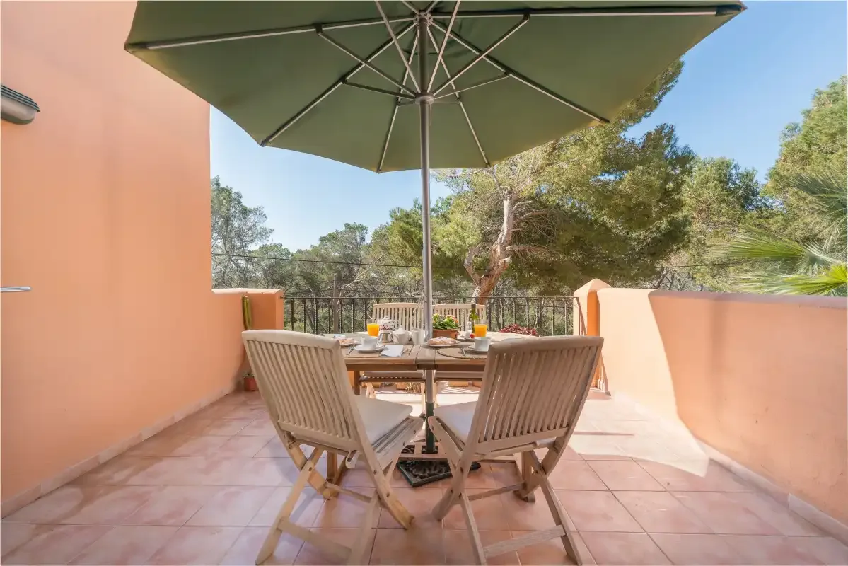 Una zona de comedor exterior con suelo de baldosas tiene una mesa y asientos bajo una gran sombrilla.