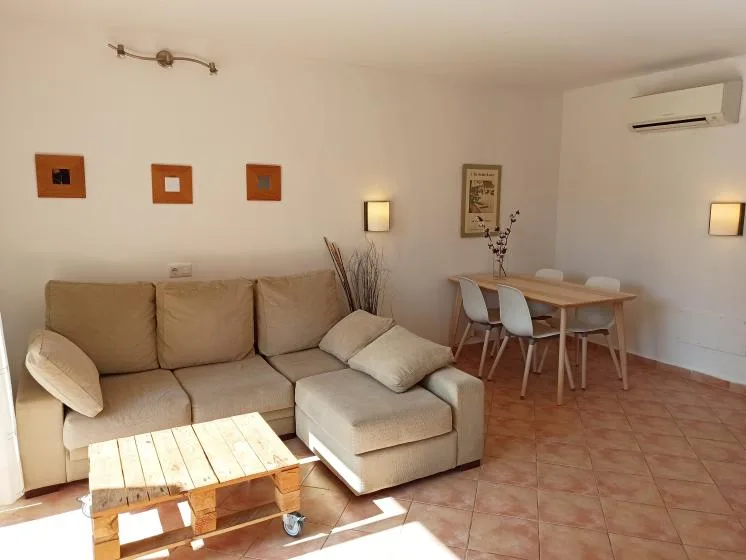 Zona de estar y comedor con asientos beige y una mesa de madera.