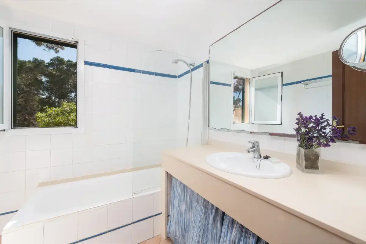Un baño con bañera, lavabo y una ventana con vistas a la vegetación.