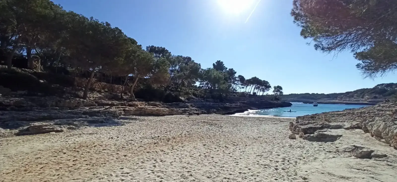 Una playa de arena bordeada de costas rocosas y árboles junto al agua.