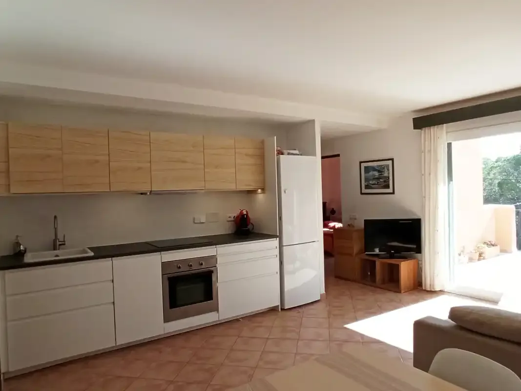 Una sala de estar con cocina abierta y un televisor junto a la ventana luminosa.