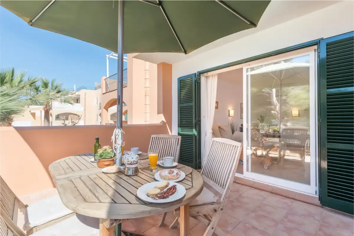 Una zona de comedor en un patio soleado, con una mesa redonda y puertas correderas abiertas.