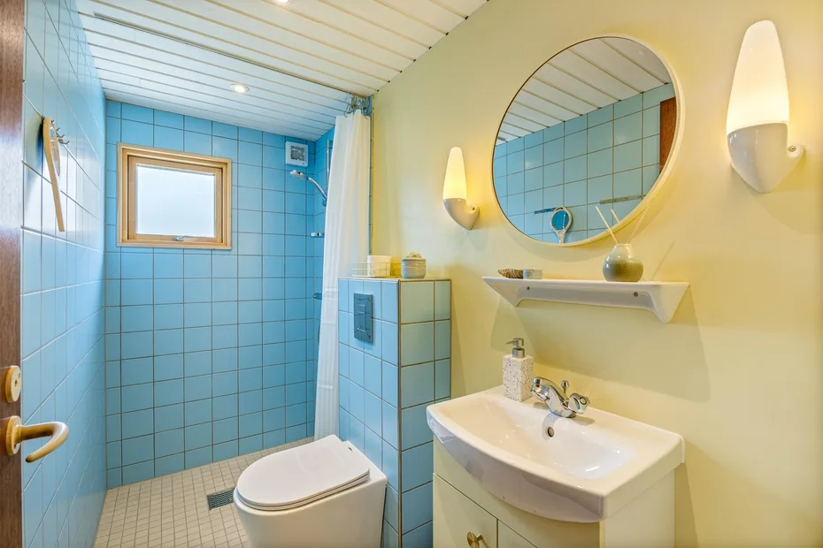 Un baño con azulejos, lavabo, inodoro y espejo redondo.
