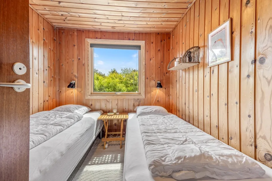 Un dormitorio revestido de madera tiene dos camas individuales junto a una ventana con vistas a la vegetación.