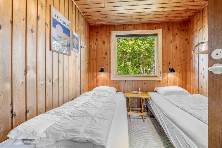 Dormitorio revestido de madera con dos camas y una ventana con vistas a la vegetación.