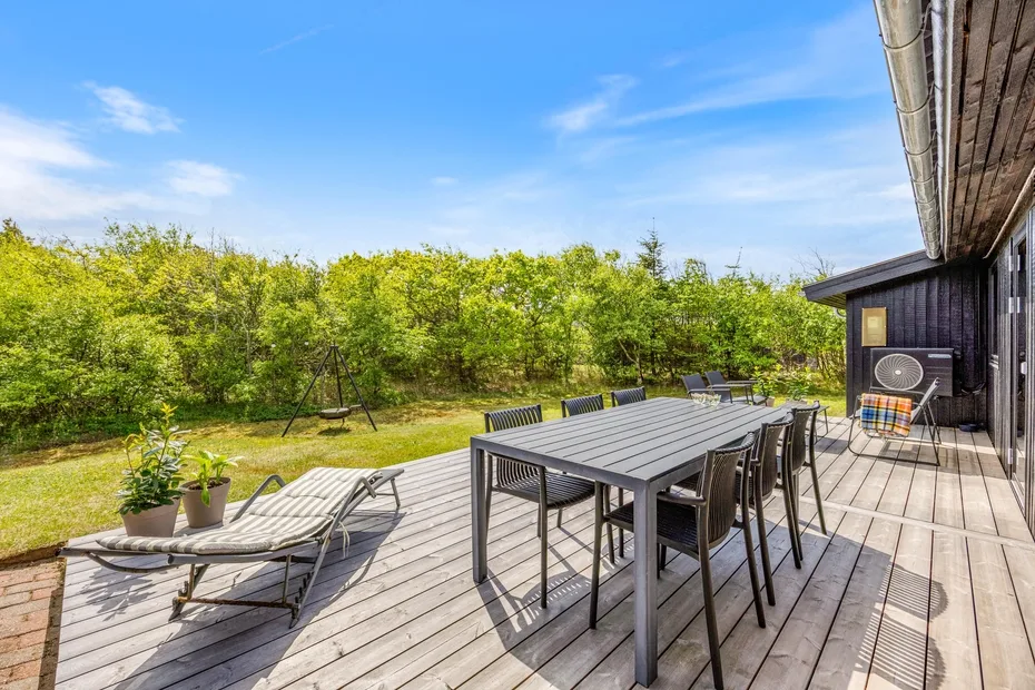 Una amplia terraza exterior con mesa de comedor, asientos y vegetación alrededor.