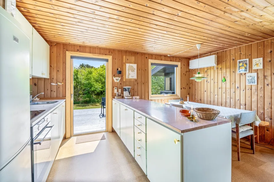 Una cocina revestida de madera con una larga encimera central y una puerta exterior abierta.