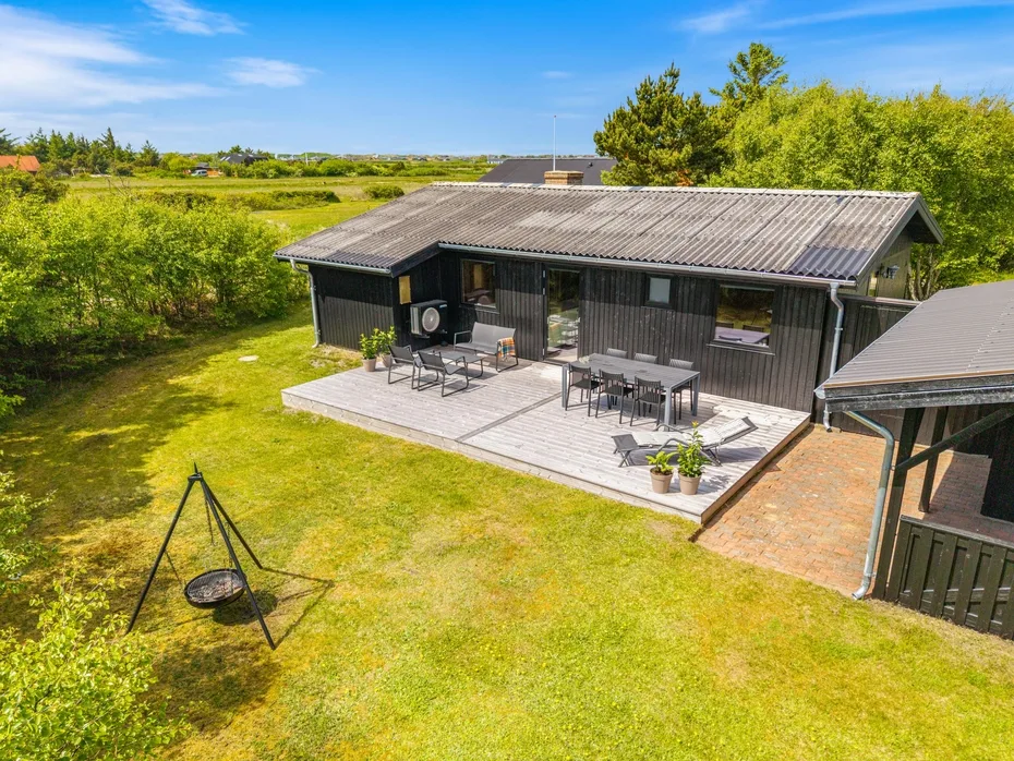 Una casa de fachada oscura tiene una amplia terraza con asientos al aire libre junto a un césped verde.