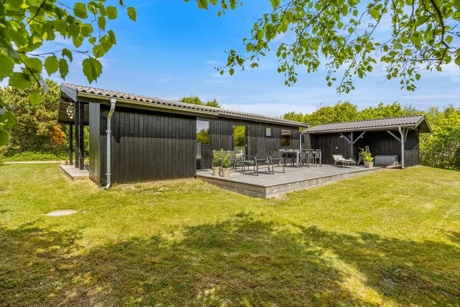 Una casa moderna se abre a un patio de madera con asientos al aire libre y césped.