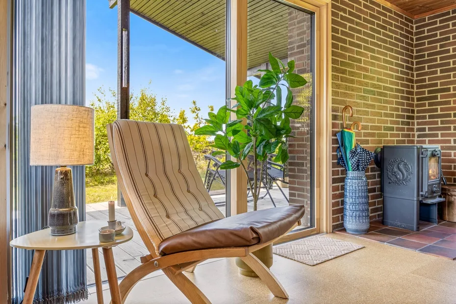 Una zona de estar con paredes de ladrillo, un sillón, una planta y grandes ventanas.