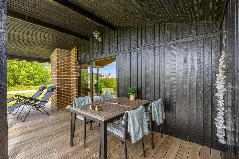 Comedor exterior cubierto con una mesa de madera junto a una pared de paneles oscuros.