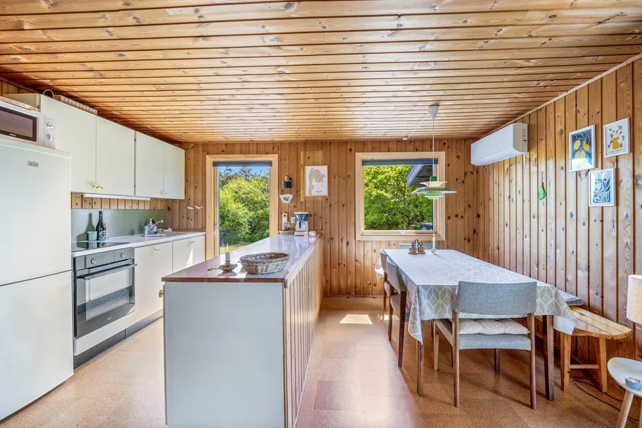 Cocina y comedor revestidos de madera, con una mesa junto a las ventanas.