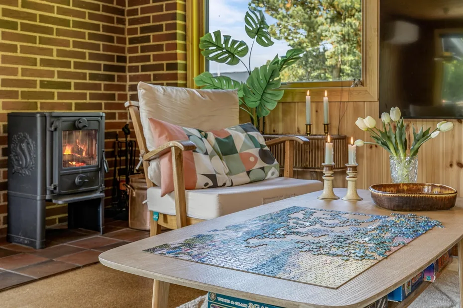 Una acogedora zona de estar tiene un sillón con cojines junto a una chimenea encendida y una mesa de centro.