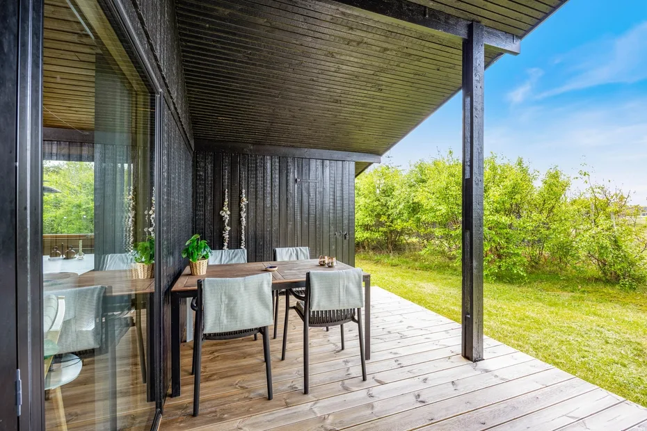 Una terraza de madera cubierta con una mesa de comedor junto a puertas corredizas de vidrio.