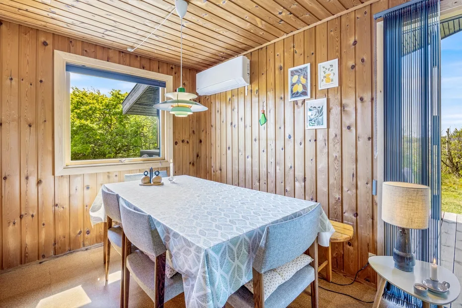 Comedor revestido de madera con una mesa, sillas y ventanas amplias.