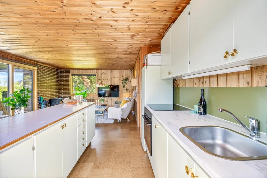 Una cocina luminosa con gabinetes blancos, una encimera larga y un comedor al fondo.