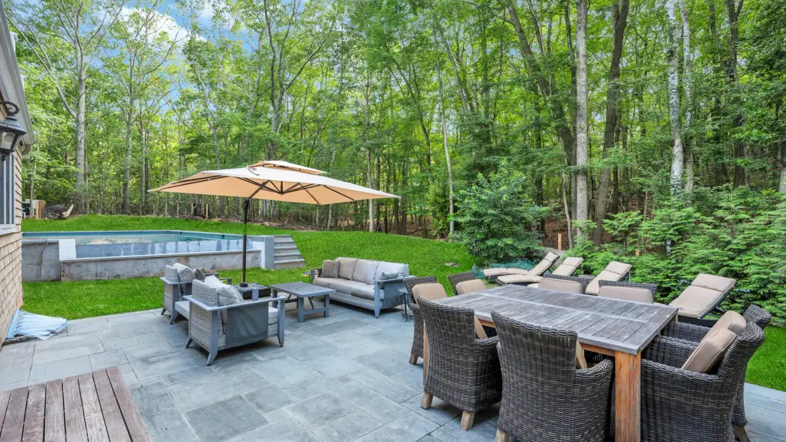 A furnished patio with outdoor seating and a dining table overlooks a wooded yard.