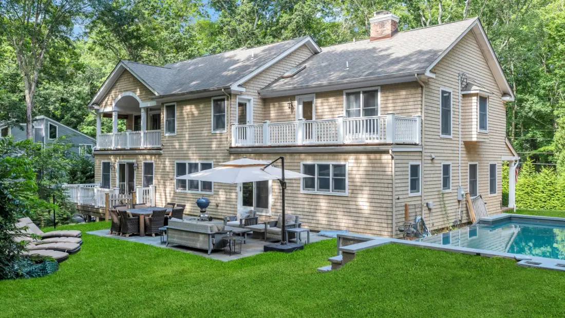 A large house with a lawn, outdoor seating, and a swimming pool.