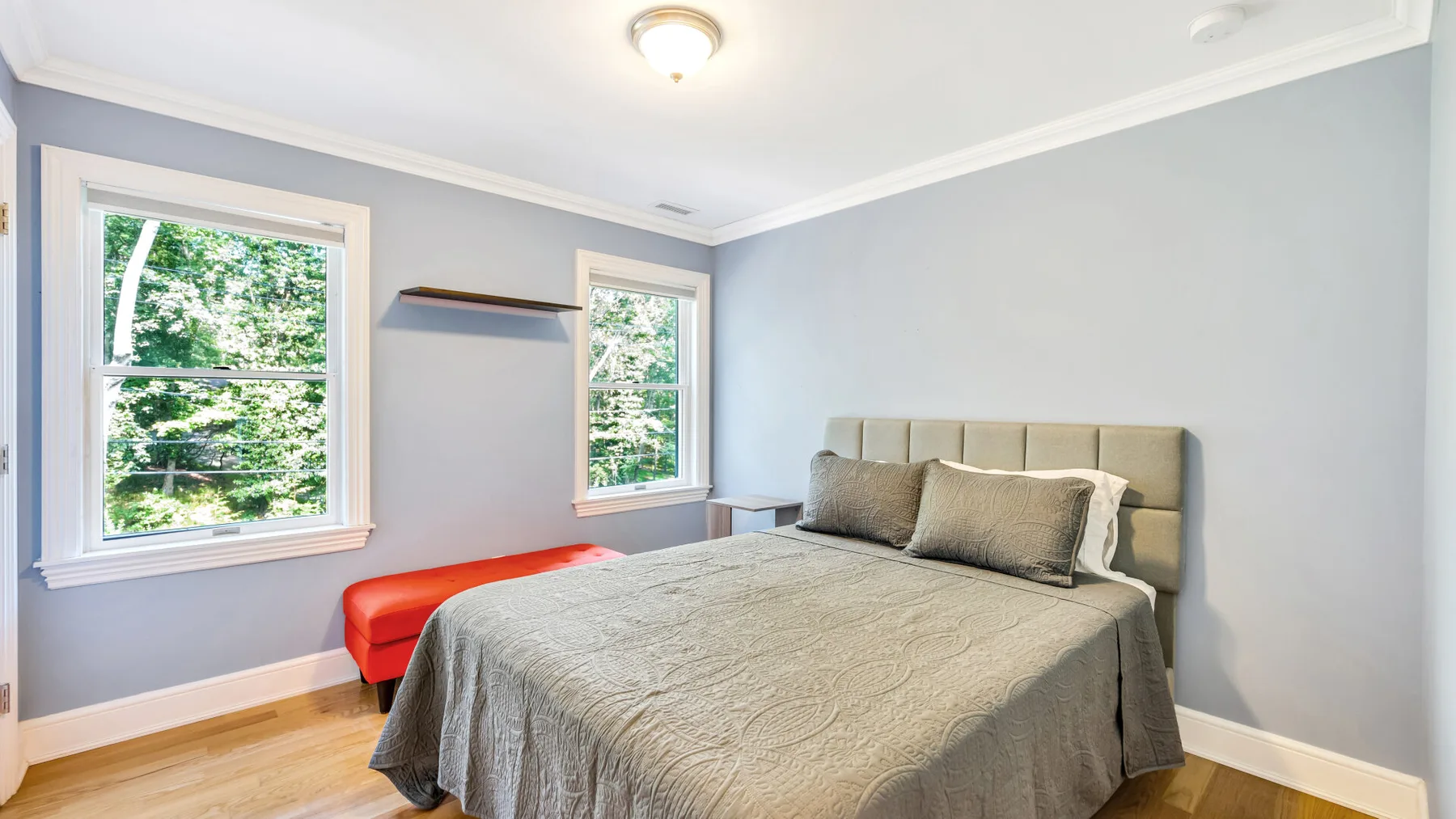 A bedroom with a bed, gray bedding, and two windows.