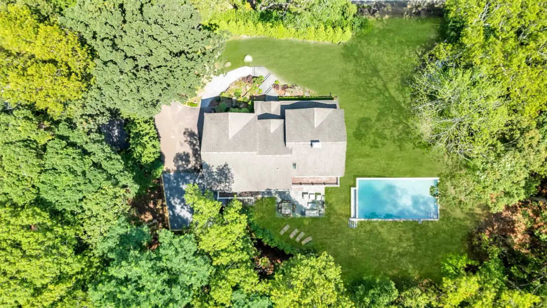 An aerial view shows a house, a swimming pool, and a lawn surrounded by trees.