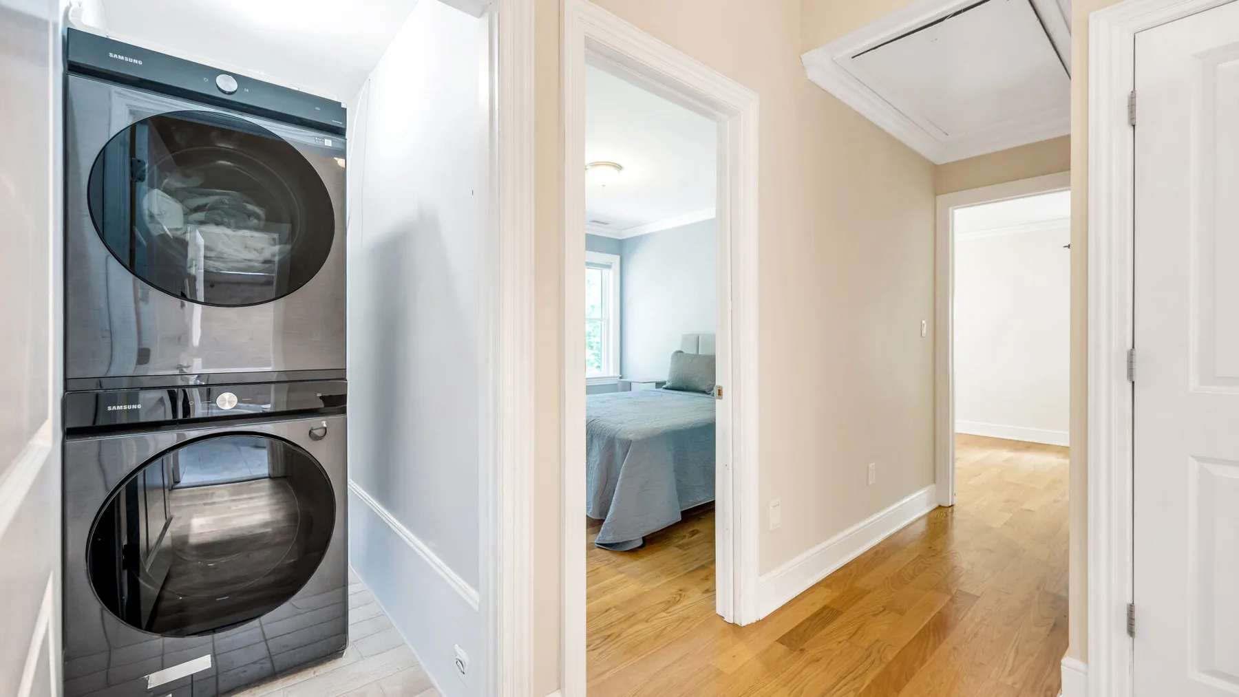 A hallway with a stacked washer and dryer beside an open bedroom doorway.