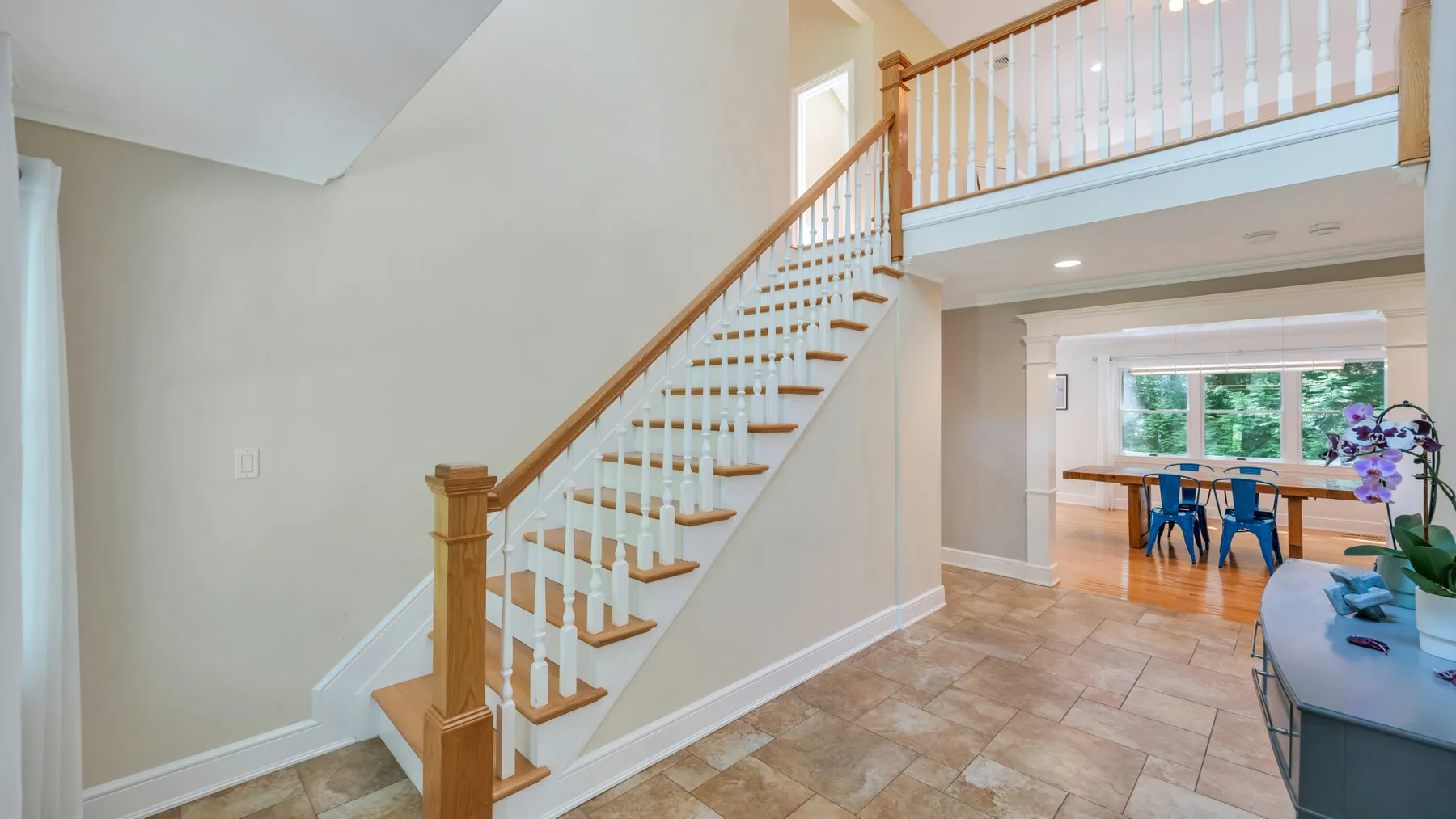 A staircase rises to an upper landing beside a dining area.