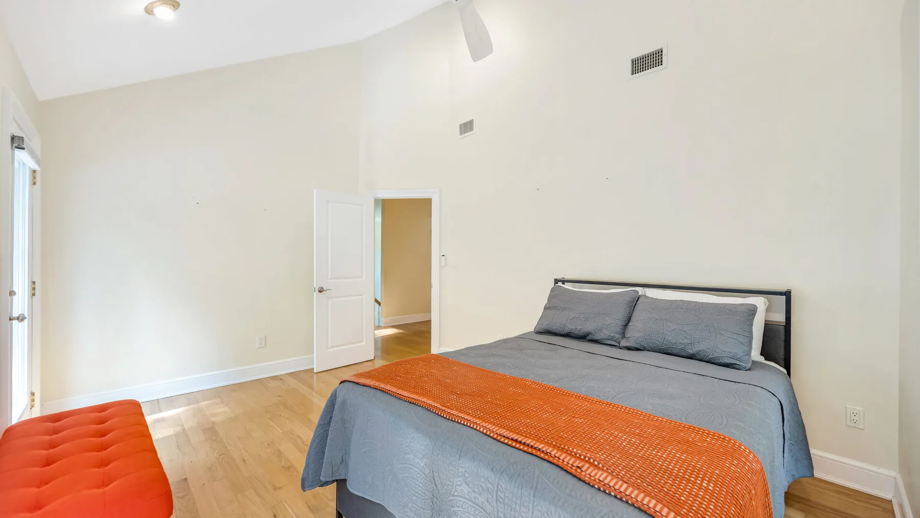 A bedroom with a bed covered in gray bedding and an orange throw.