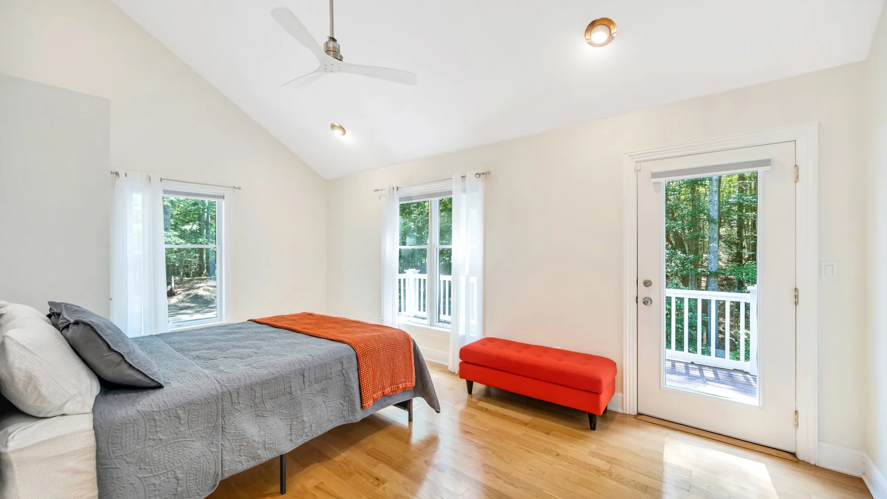 A bright bedroom with a bed, a red bench, and a glass door overlooking greenery.