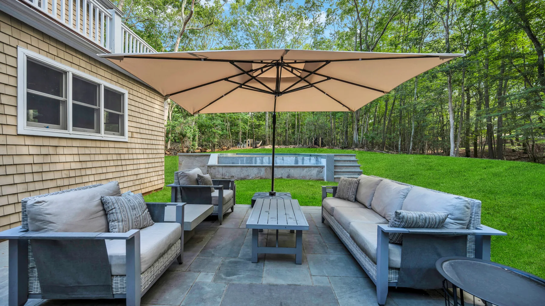An outdoor patio has seating arranged around a low table beneath a large umbrella.